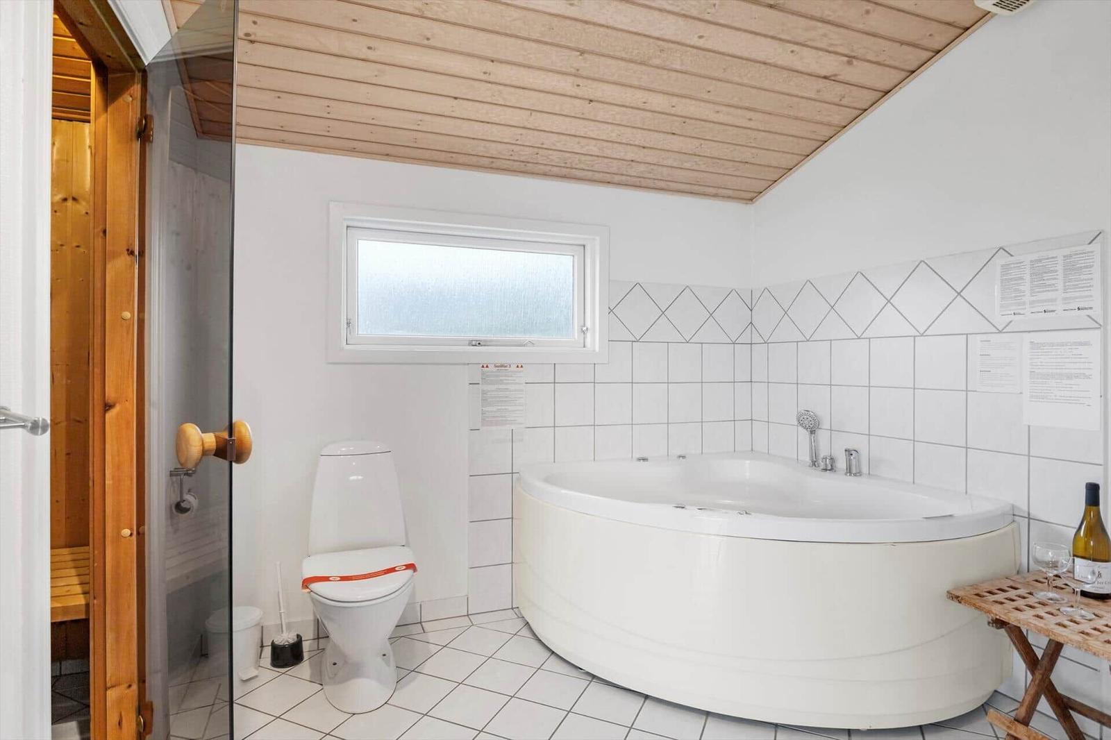 Badezimmer mit Whirlpool, Toilette und Sauna. Holzdecke und Fliesenwand.