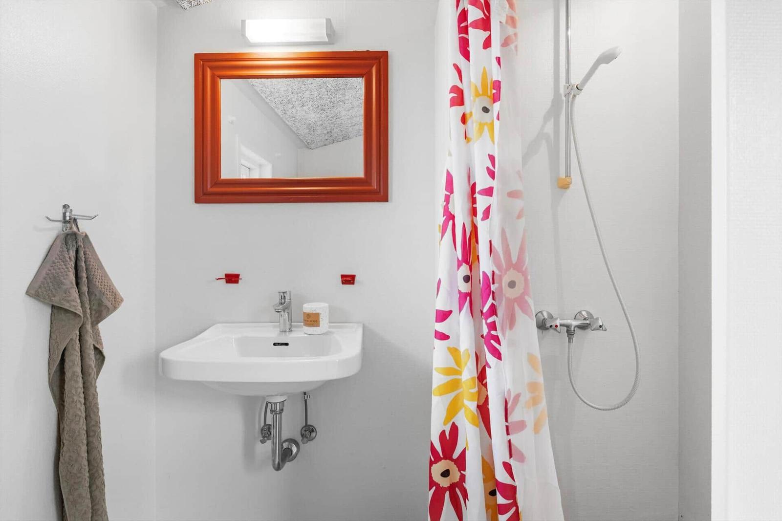 Badezimmer mit Waschbecken, Spiegel und Dusche mit buntem Vorhang.