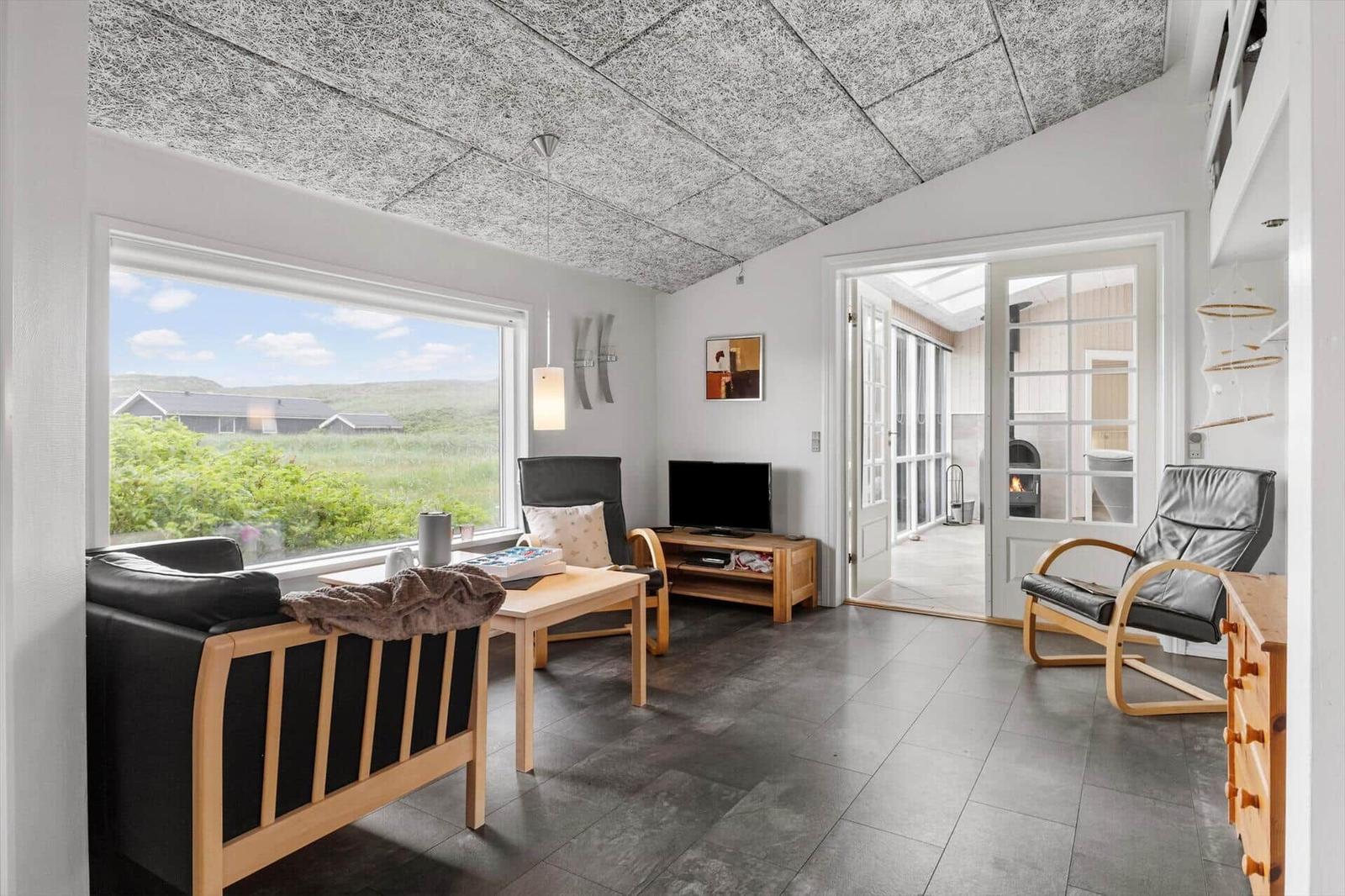 Wohnzimmer mit großem Fenster, Sitzmöbeln und Blick auf Landschaft.