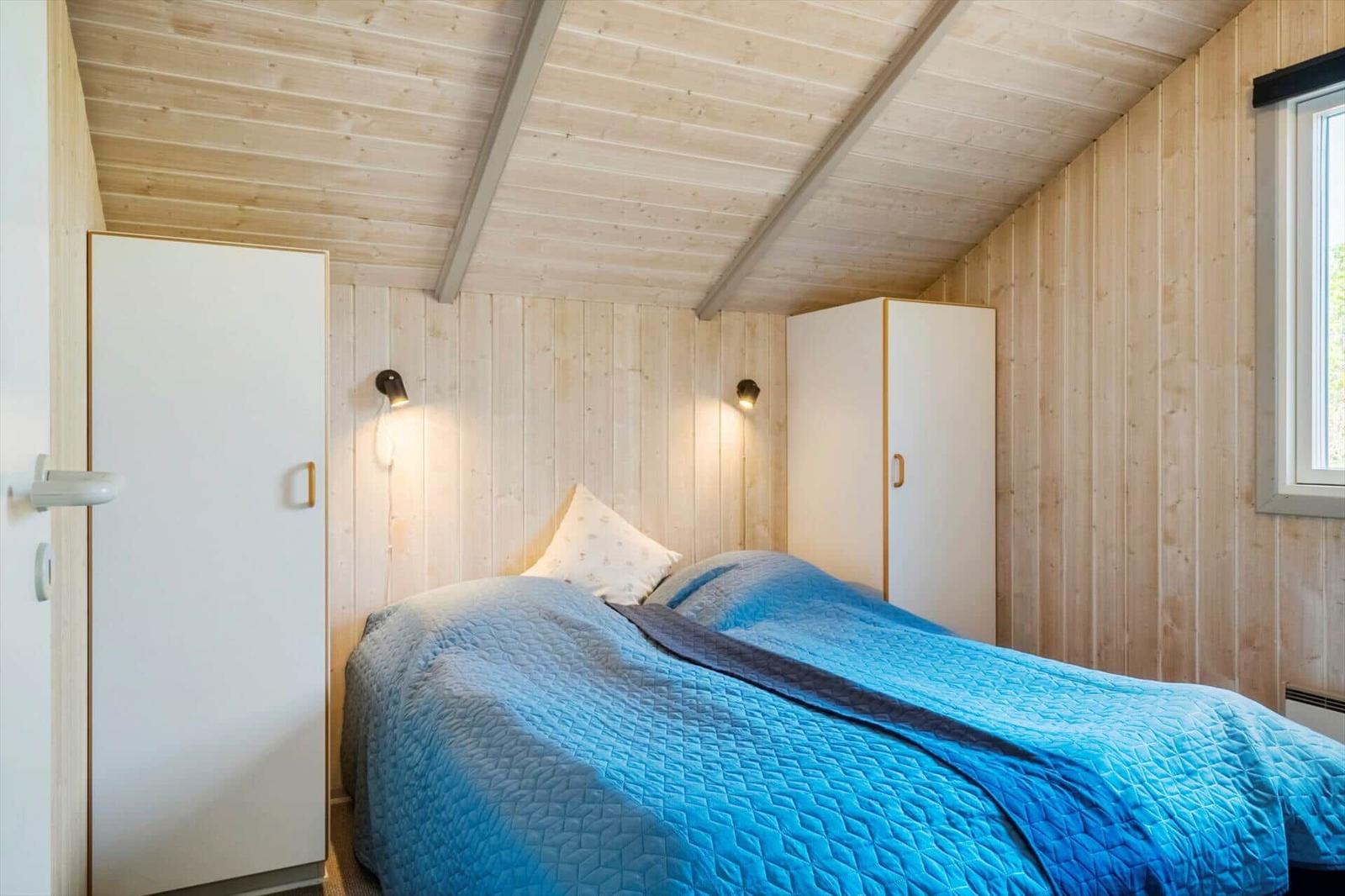 Schlafzimmer mit Holzwand, Bett und zwei Schränken. Decke mit Holzbalken.
