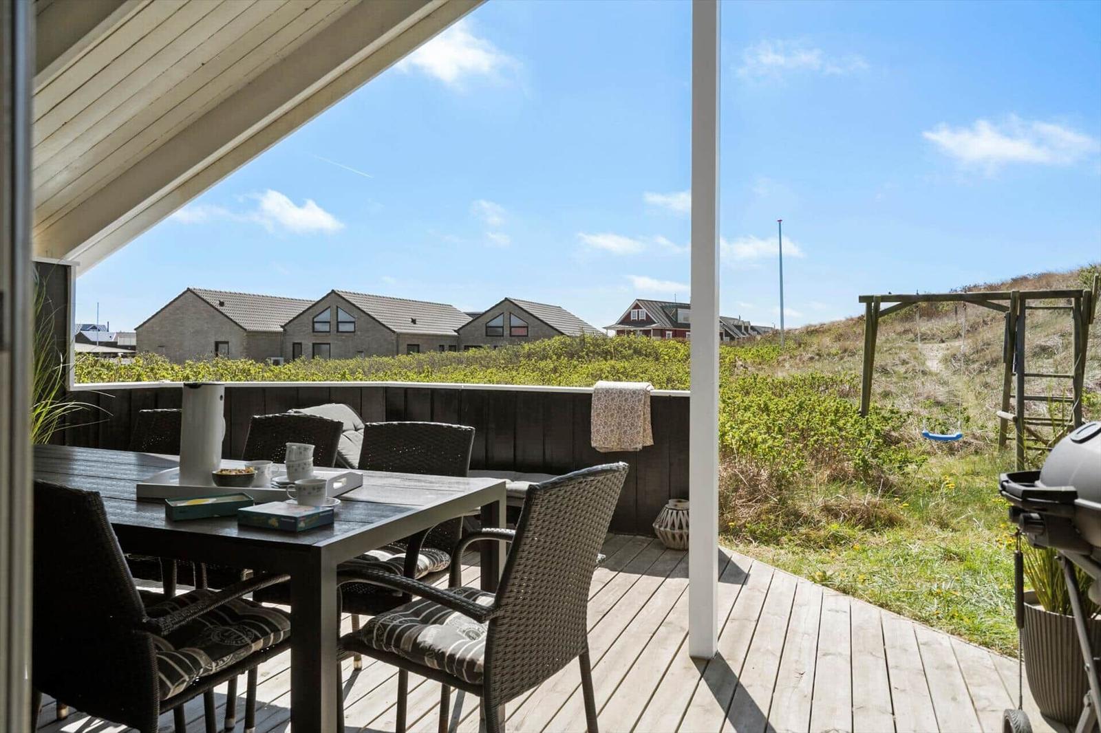 Terrasse mit Tisch, Stühlen und Grill. Blick auf Grünflächen und Häuser.