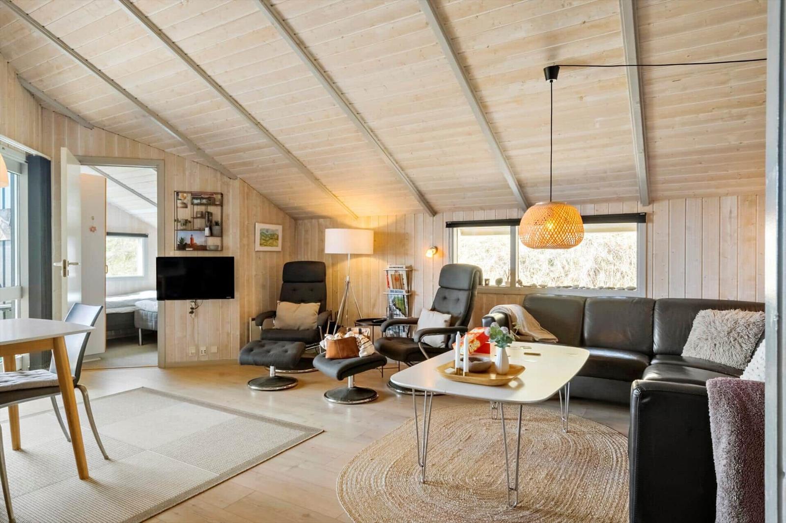 Wohnzimmer mit Sofa, zwei Sesseln, Tisch und Fernseher. Holzwände und -decke.
