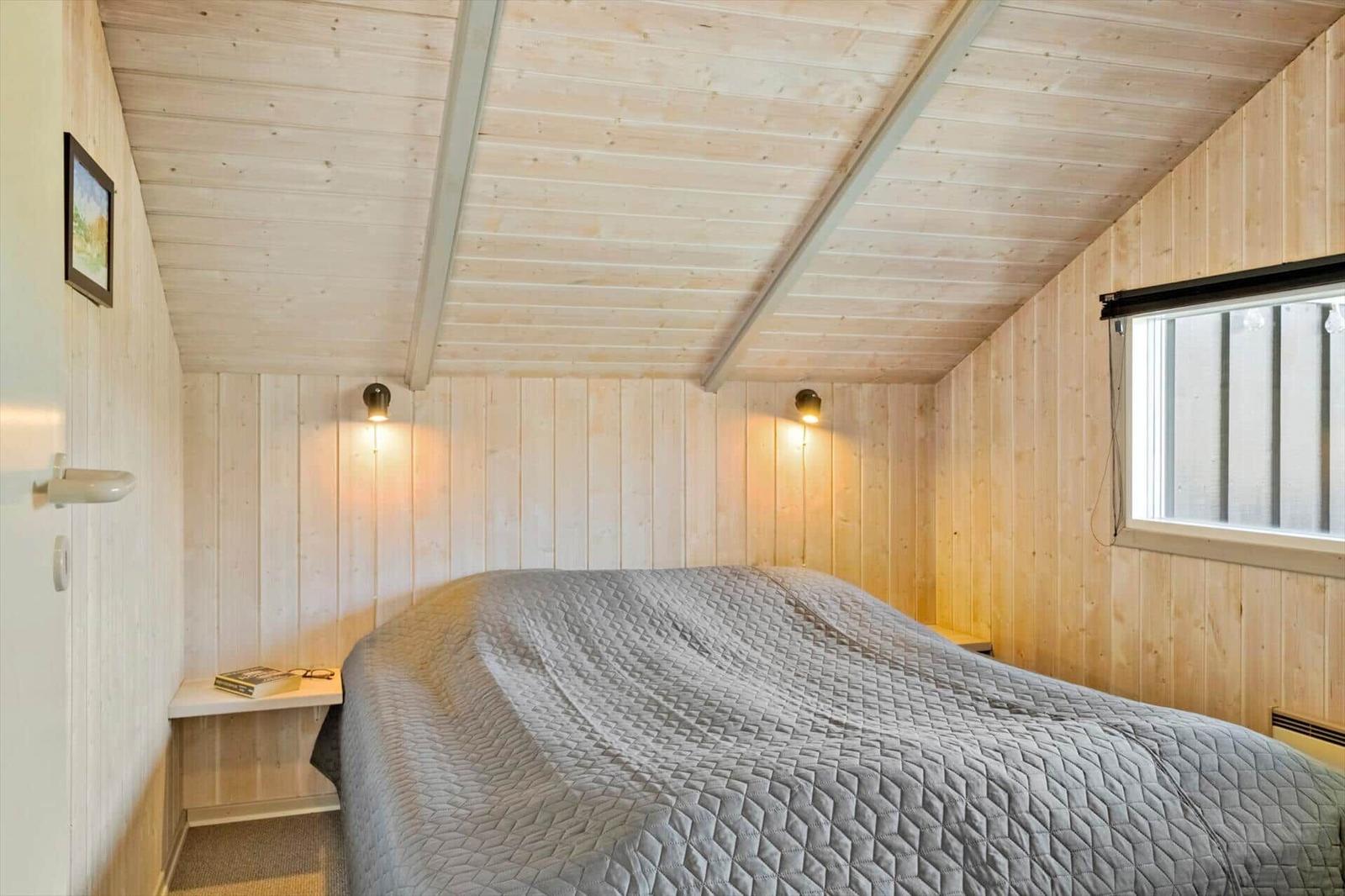Schlafzimmer mit Holzwänden, Bett und Fenster.