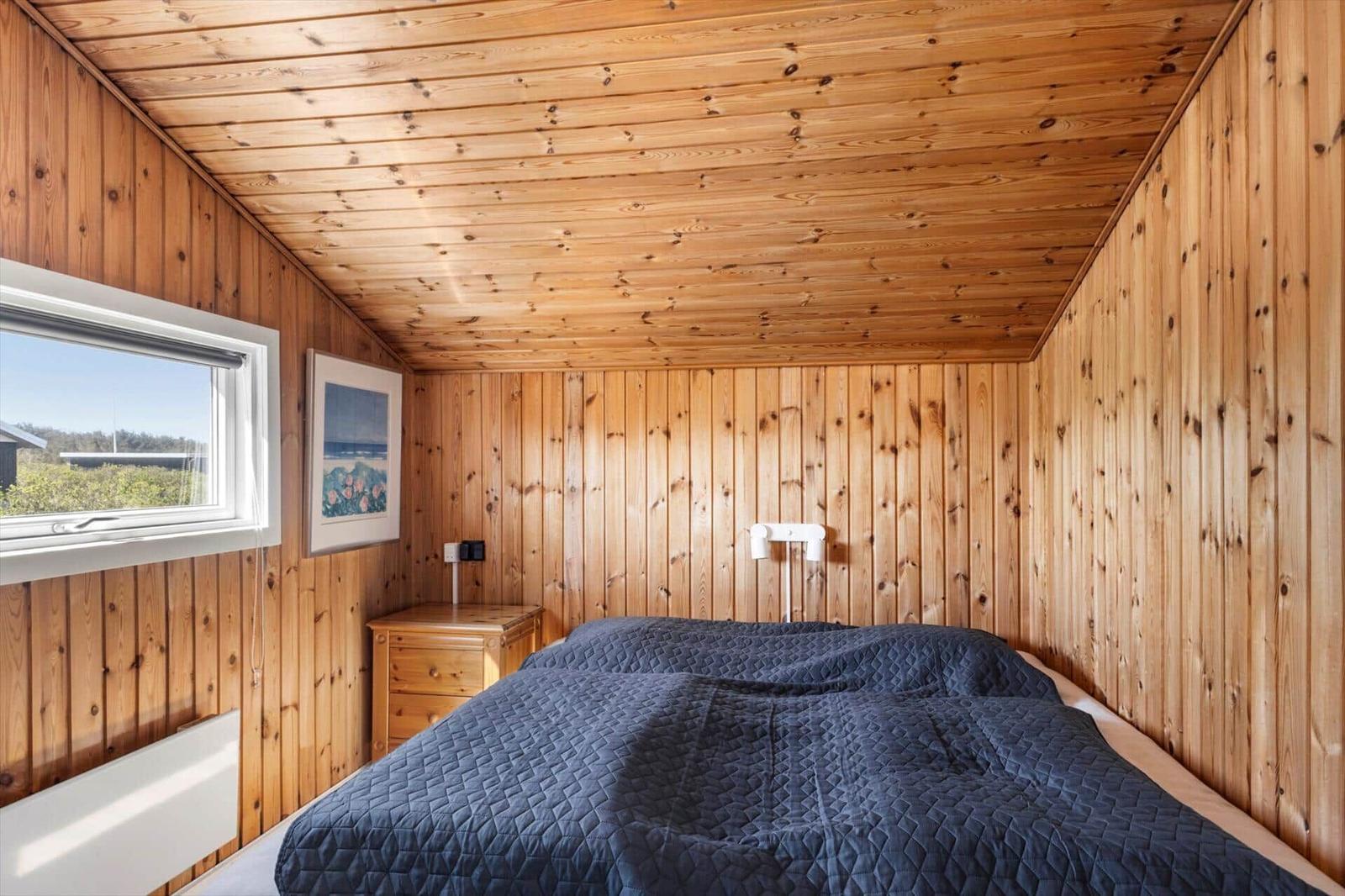 Schlafzimmer mit Holzwand, Bett und Fenster. Wandbild und Nachttisch sichtbar.