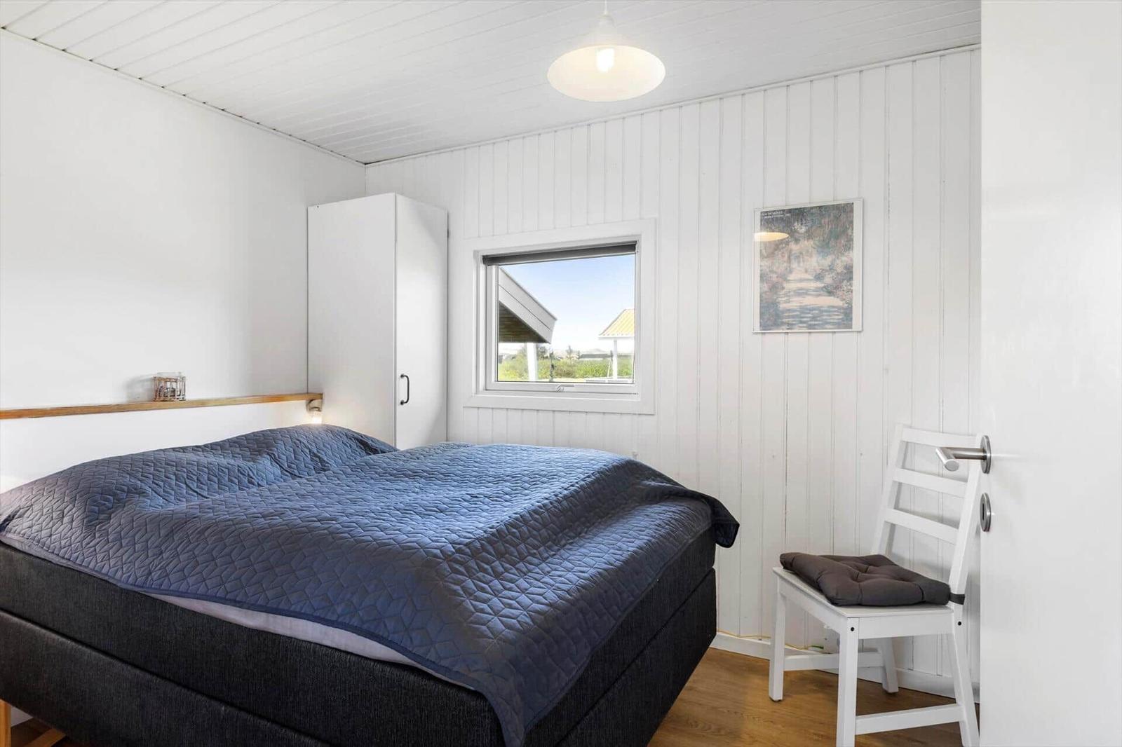 Schlafzimmer mit Bett, Kleiderschrank und Fenster. Weiße Wände und Holzboden.