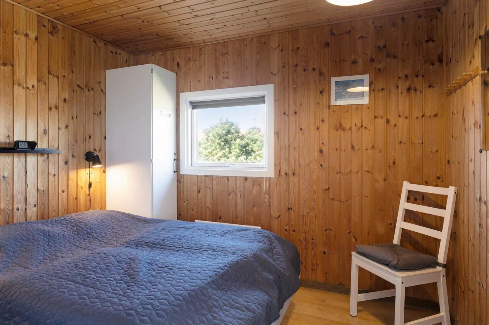 Schlafzimmer mit Holzwänden, Bett, Stuhl und Fenster.