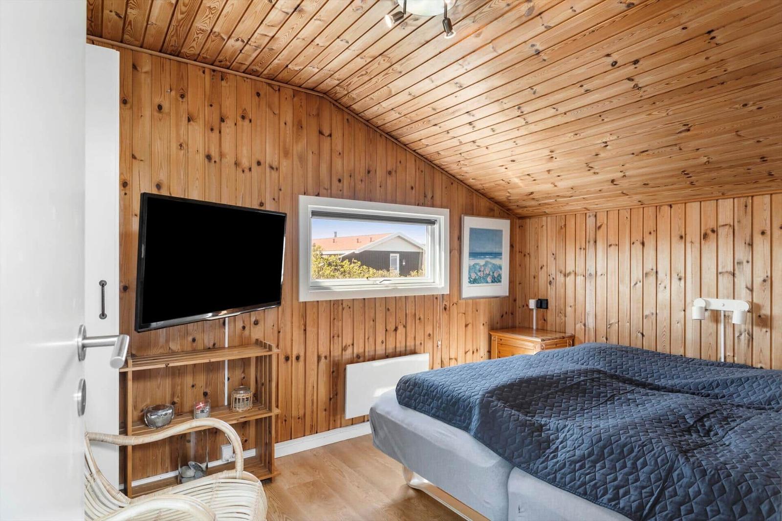 Schlafzimmer mit Holzwand, Bett, Fernseher und Fensterblick.