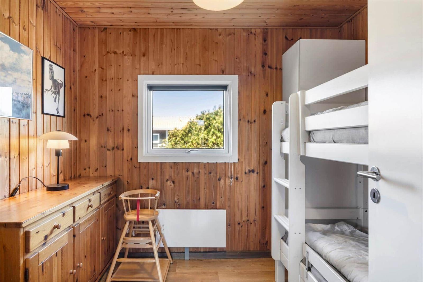 Schlafzimmer mit Doppelstockbett, Holzwand und Fenster mit Blick auf Grün.