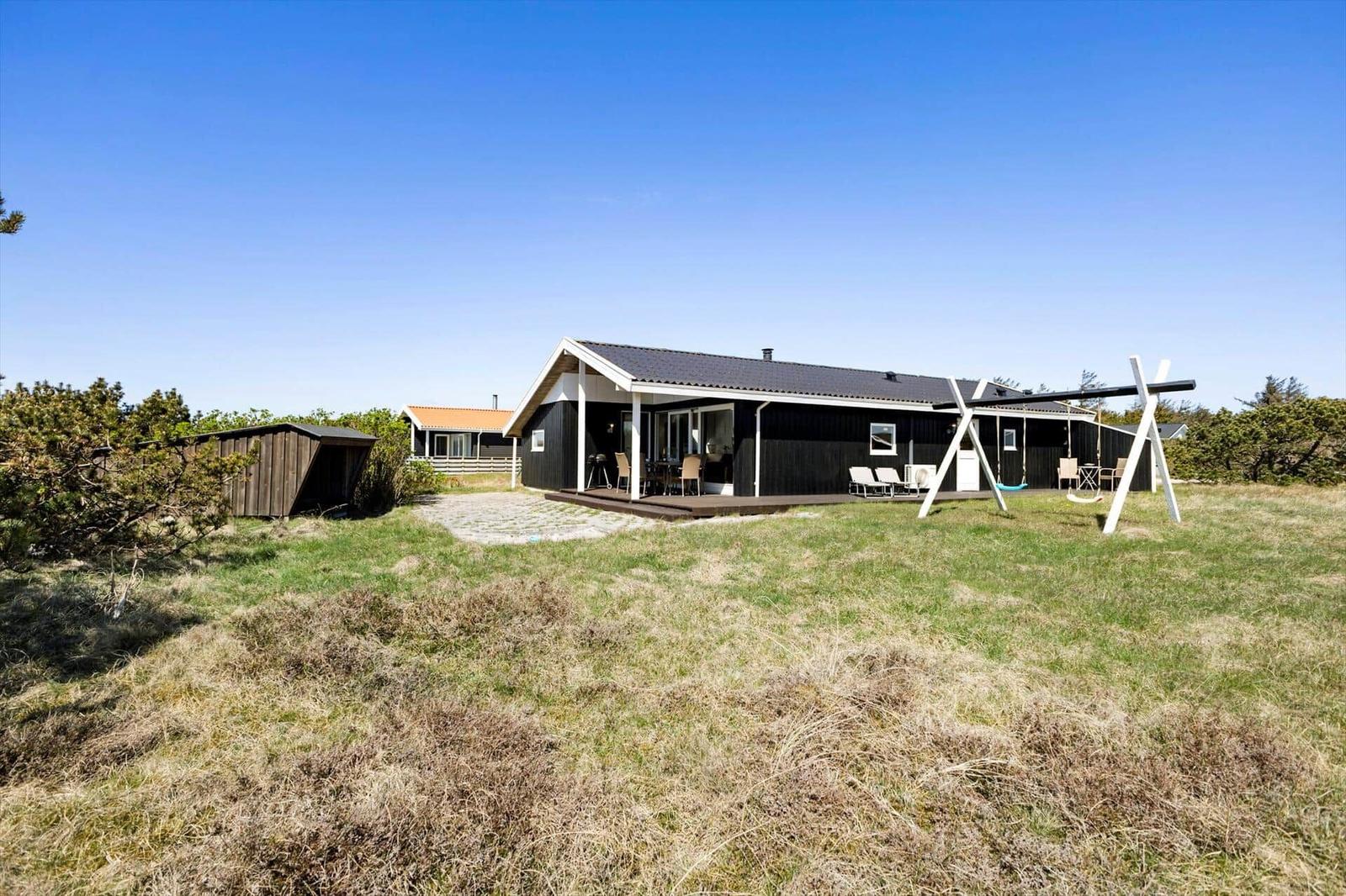 Schwarze Hütte mit Terrasse und Garten. Spielplatz und Grillplatz vorhanden.