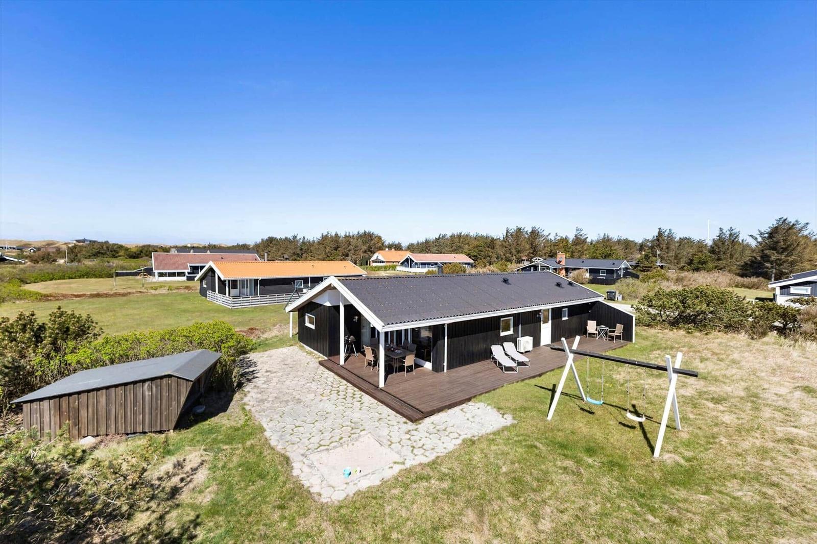 Moderne Ferienhaus mit Terrasse, Schaukel und Garten. Hintergrund: Grünfläche und andere Häuser.
