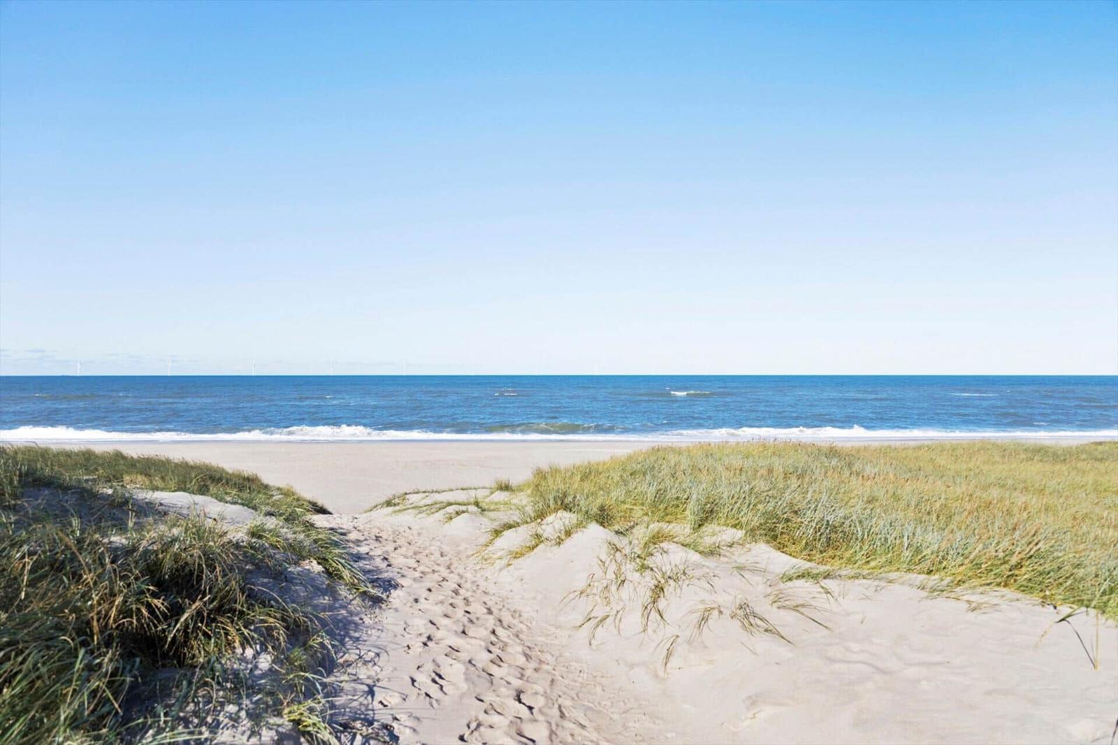 Wanderweg durch Sanddünen zum Strand mit Blick auf das Meer und Windkraftanlagen.