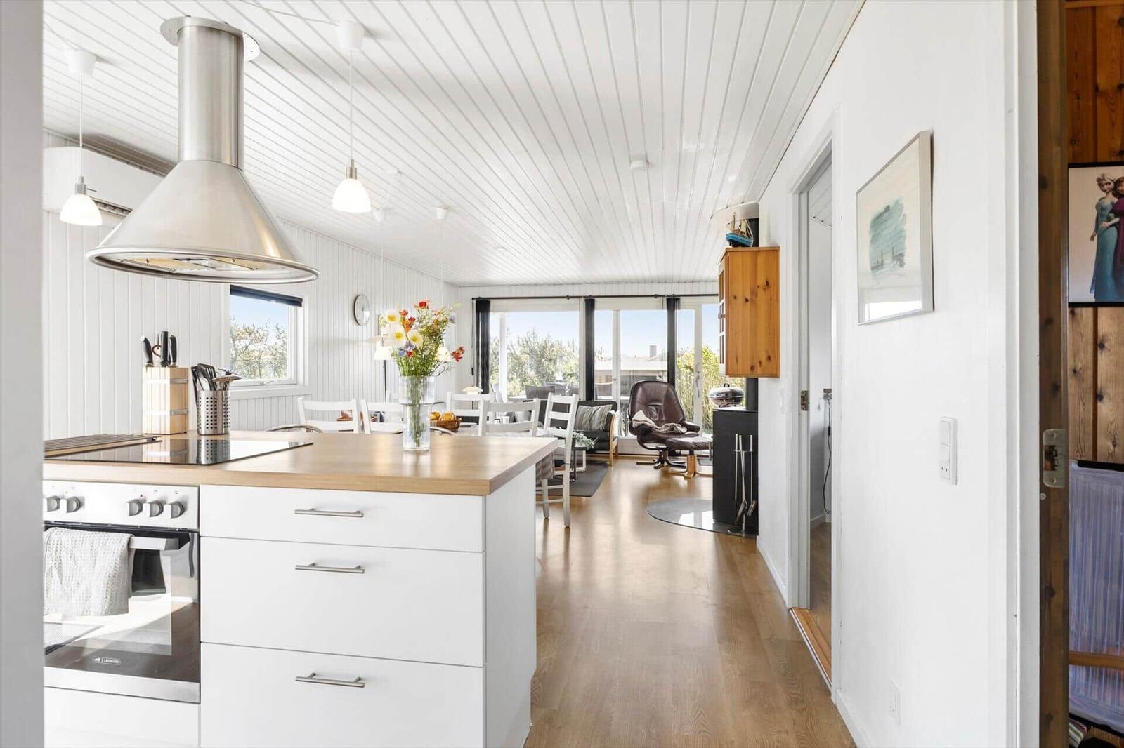 Küche mit Insel und Essbereich, Blick in Wohnzimmer mit Sessel und Fenstern.