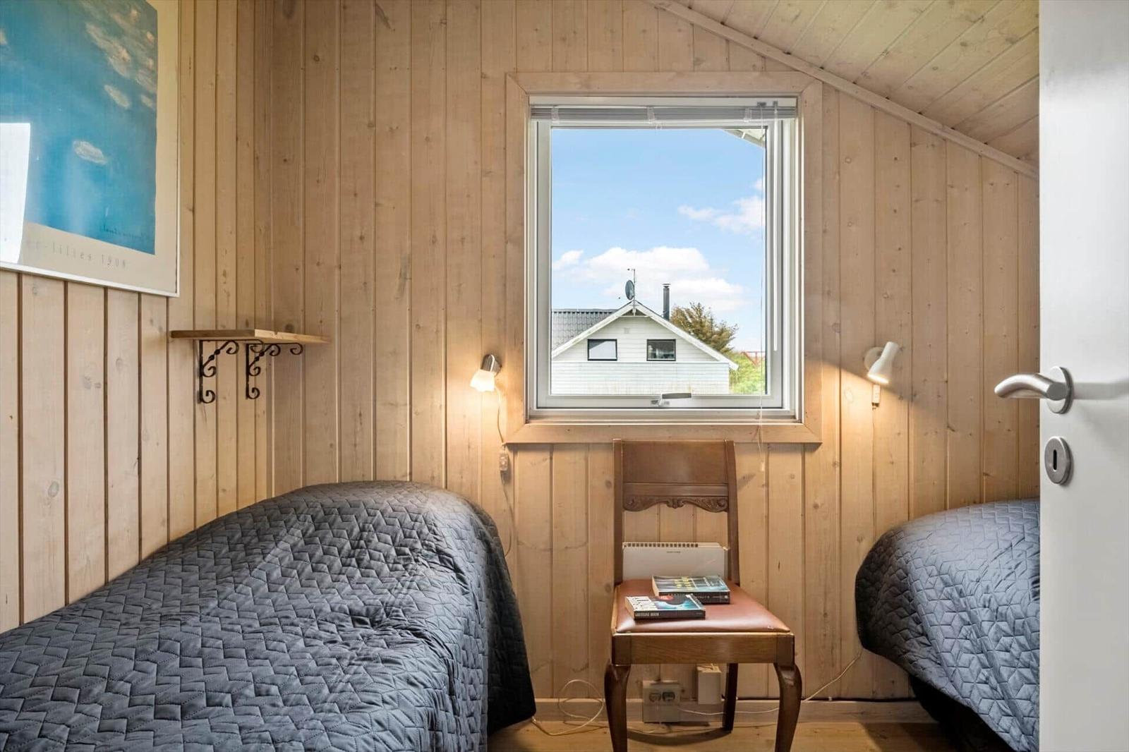 Zwei Betten mit dunkler Bettwäsche, Holzwände und ein Fenster mit Blick auf ein Haus.