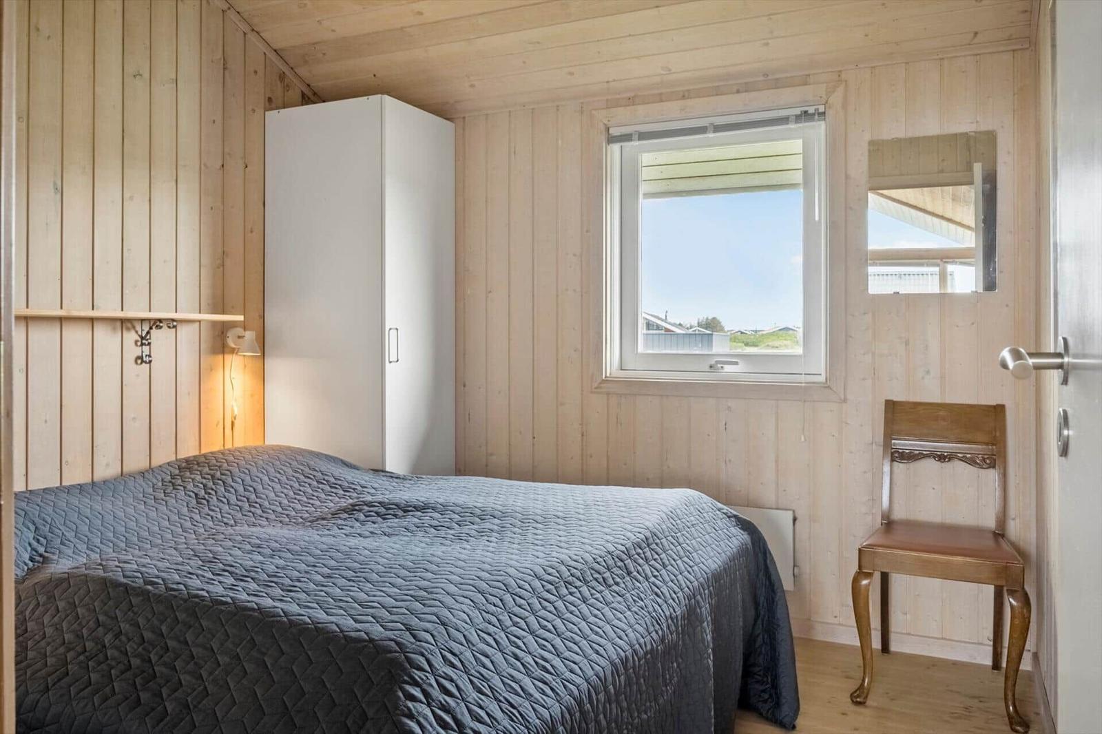 Schlafzimmer mit Bett, Kleiderschrank, Stuhl und Fenster. Wände und Decke sind holzverkleidet.