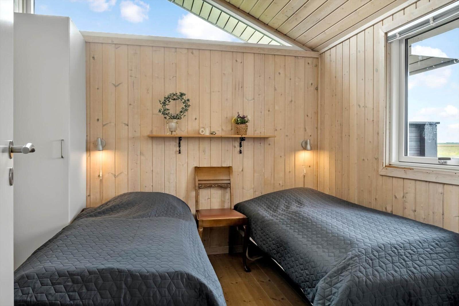 Zwei Betten mit dunklen Bettdecken, Holzwand und Dachfenster.