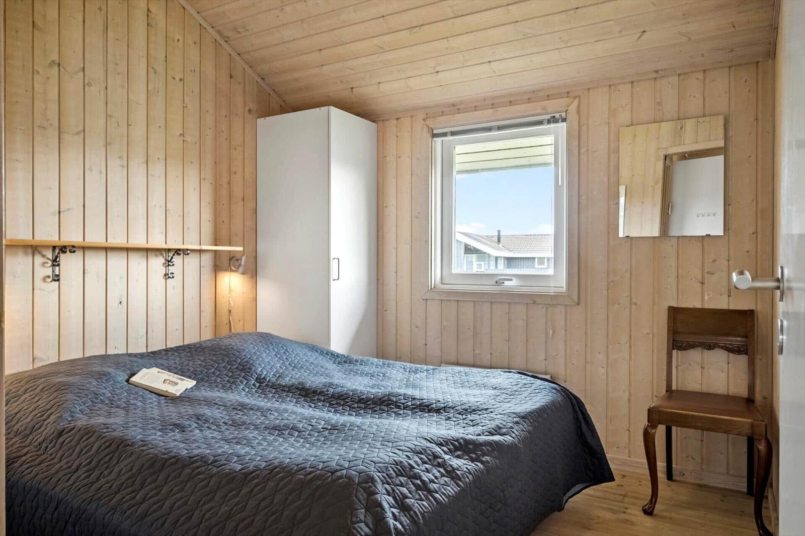 Schlafzimmer mit Holzwand, Bett, Schrank, Stuhl und Fenster