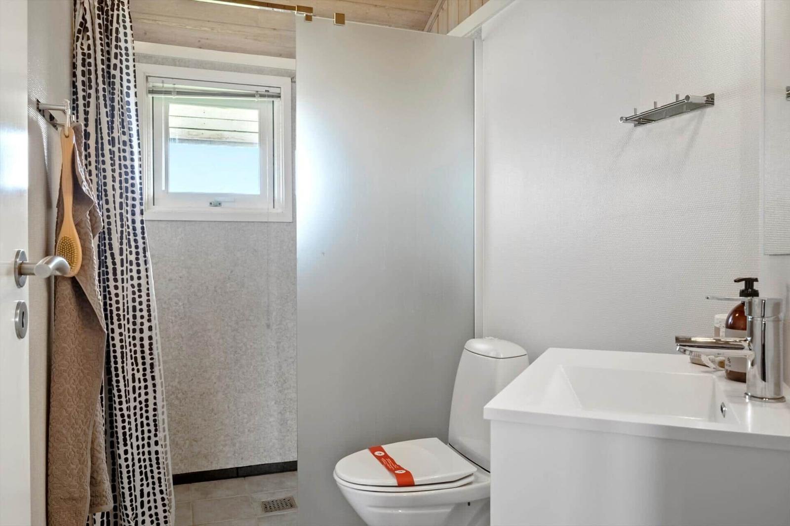 Badezimmer mit Toilette, Waschbecken und Dusche mit Fenster.