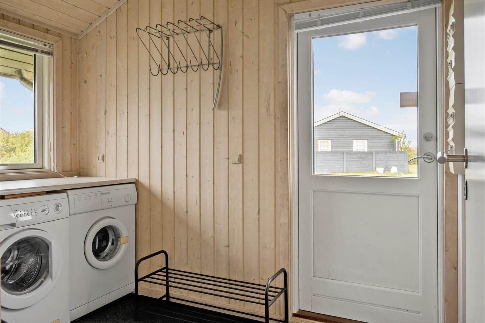 Waschraum mit Waschmaschine, Trockner und Fenster. Holzwand und Tür zum Außenbereich.