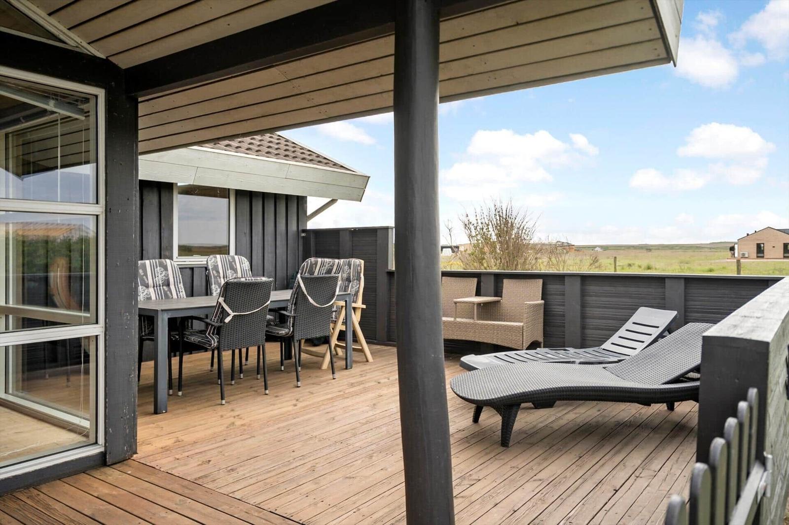 Terrasse mit Sitzgelegenheiten und Liegen. Blick auf grünes Feld unter blauem Himmel.