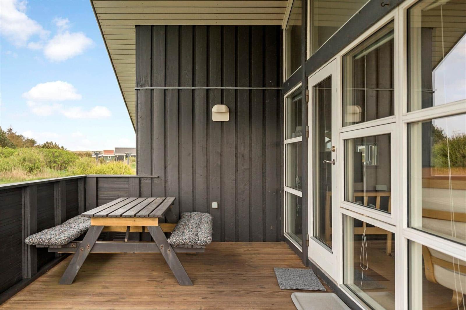 Terrasse mit Holztisch und Sitzbänken, Blick auf Grünland und Himmel.