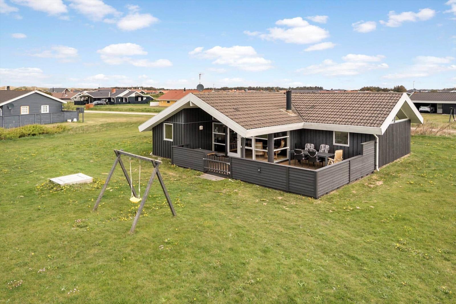 Ein Haus mit Terrasse und Schaukel im Gras. Hintergrund: weitere Häuser.