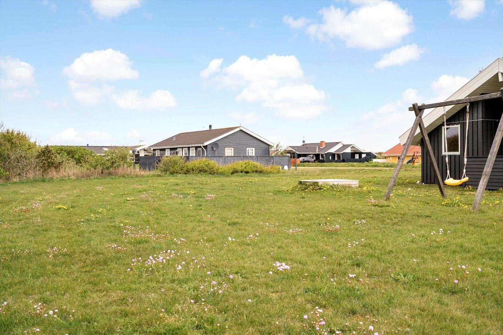 Grünes Grundstück mit Schaukel und mehreren Häusern im Hintergrund unter blauem Himmel.