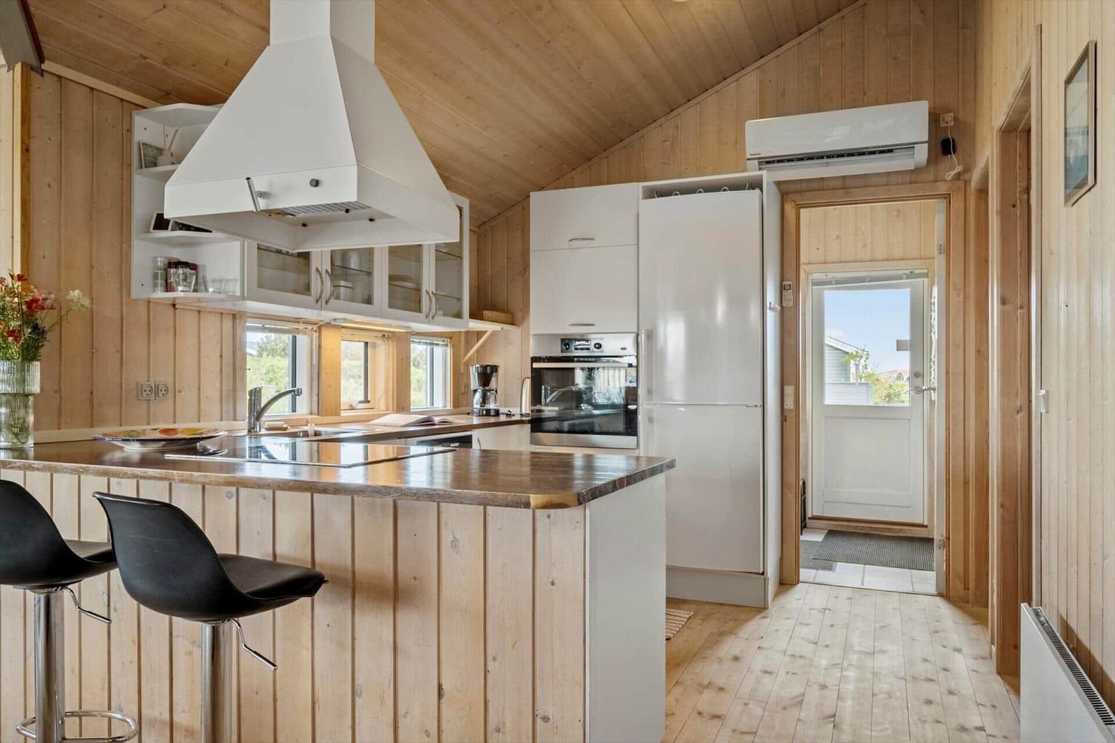 Küche mit Holzwand, weißen Schränken, Kühlschrank und Kücheninsel mit Barhockern.