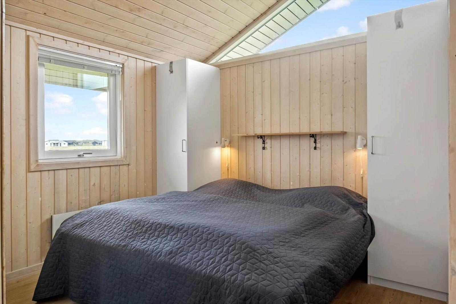 Schlafzimmer mit Doppelbett, Holzwand und Dachfenster. Fenster zeigt Außenansicht.