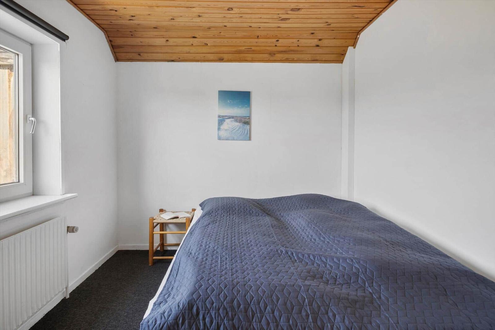 Schlafzimmer mit Holzdecke, blauem Bett und Wandbild.