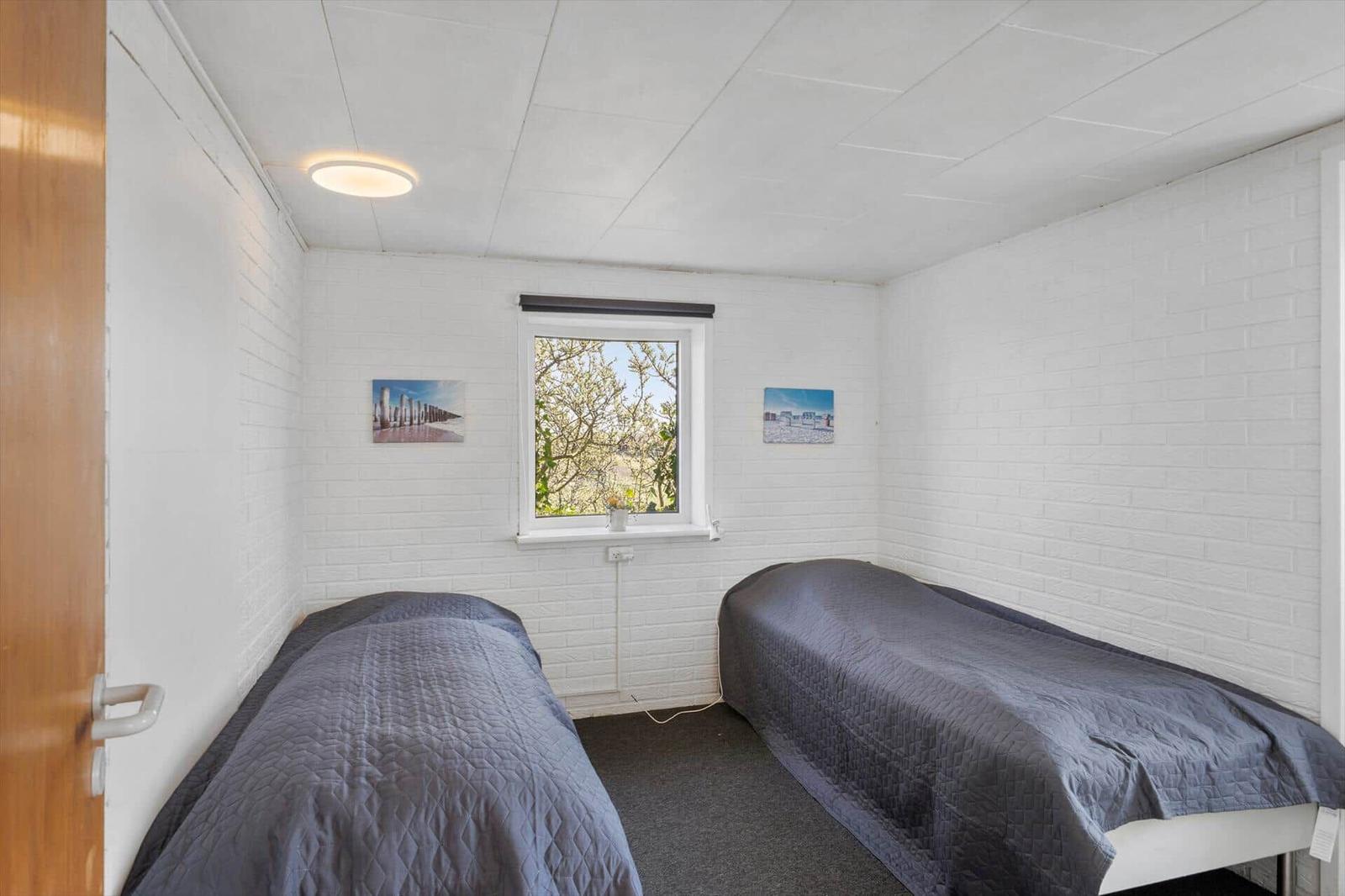 Zwei Betten in einem Raum mit weißer Wand und Fenster. Wandbilder und Deckenleuchte.