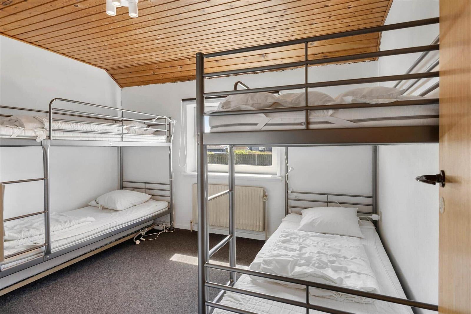 Zimmer mit zwei Doppelstockbetten, Holzdecke und Fenster.
