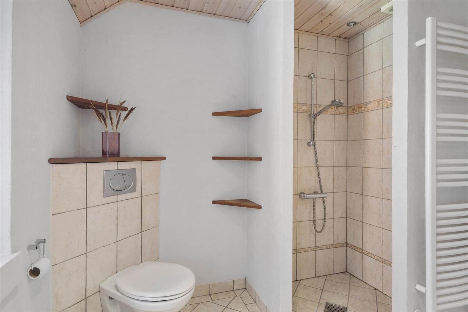 Badezimmer mit Dusche, Toilette und Holzregalen an der Wand.