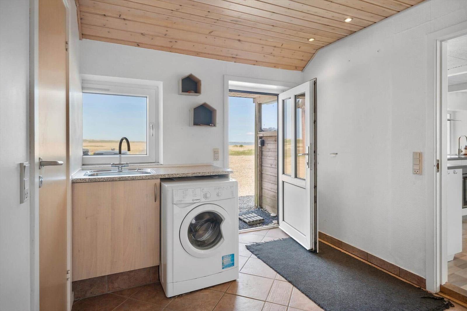 Wohnraum mit Waschmaschine, Fenster und Tür zum Außenbereich.