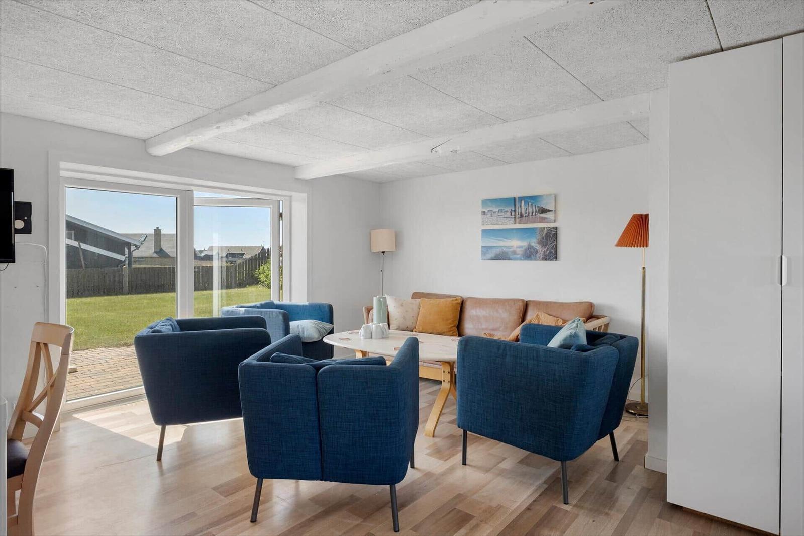 Wohnzimmer mit blauen Sesseln, Sofa und Tisch. Durchgangstür zum Garten. Decke mit Balken.
