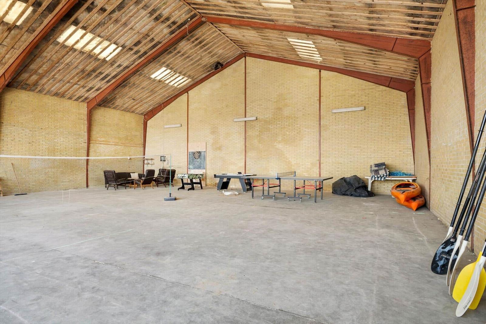Großer Hallenbereich mit Tischtennis, Volleyballnetz und Kajak- sowie Rudergerät.