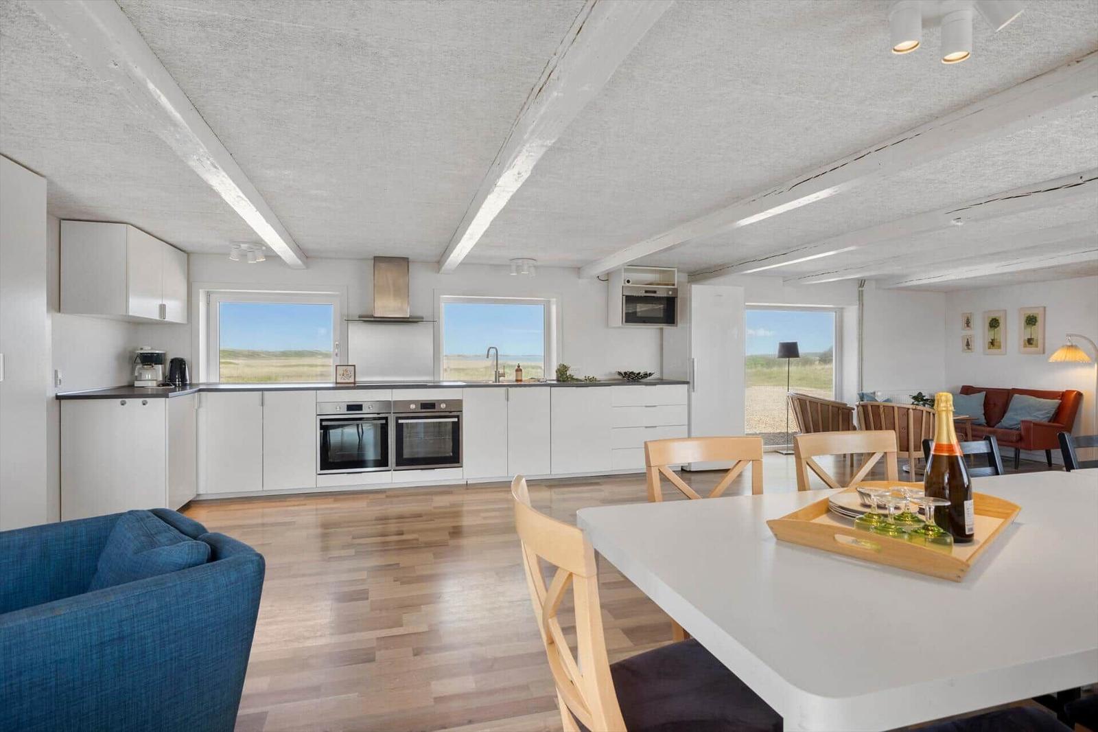 Küche mit Essbereich und Wohnzimmer. Holzboden, weiße Schränke und große Fenster.
