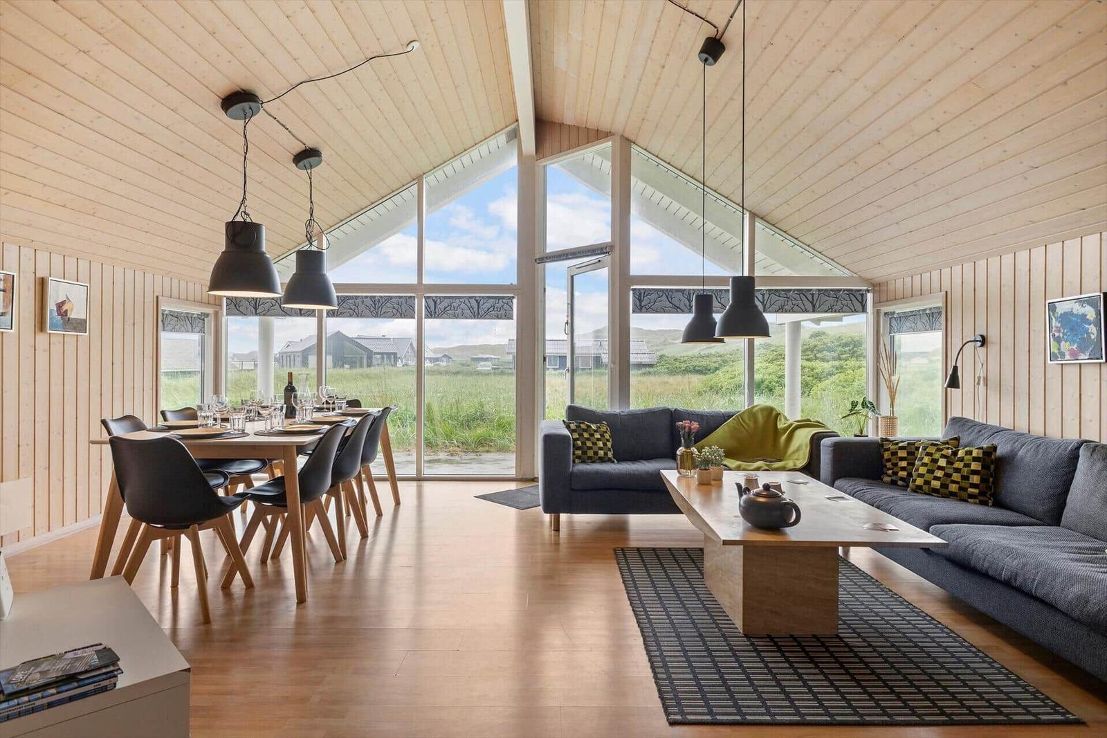 Wohn- und Essbereich mit Holzdecke, großen Fenstern und moderner Einrichtung.