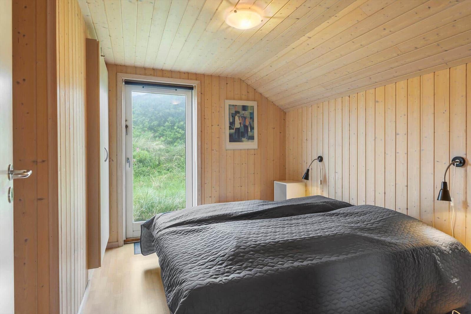Schlafzimmer mit Holzwand, Bett und Fenster zur grünen Landschaft.