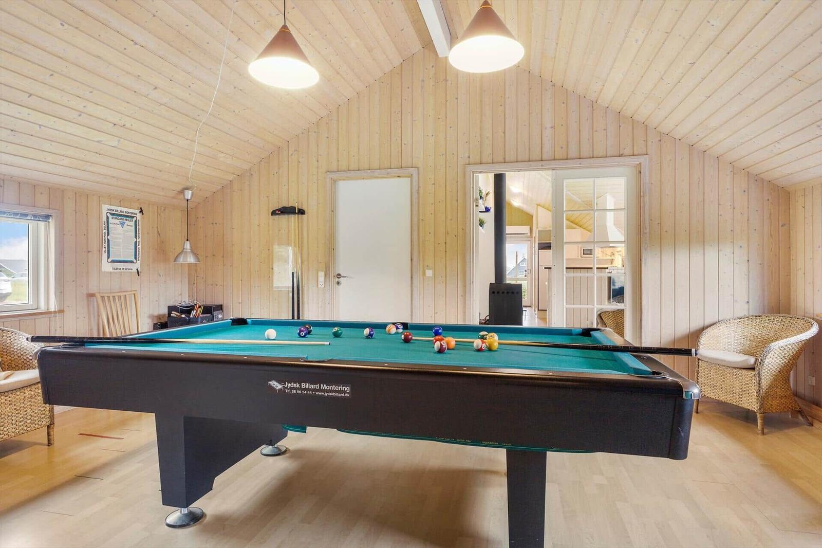 Billardtisch mit Bällen in Holzraum mit Sesseln und Fenster