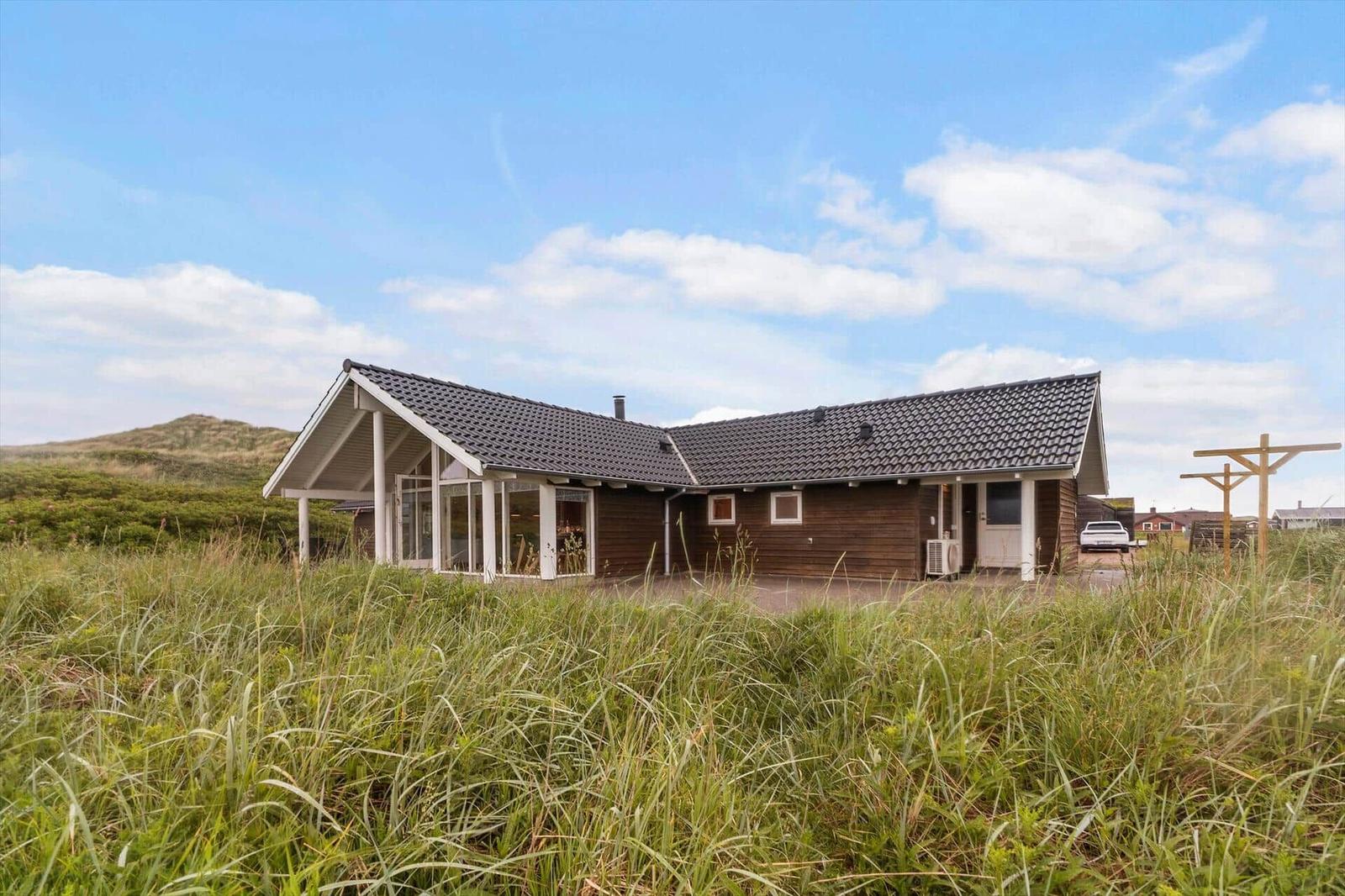 Holzhaus mit Dach und Fenstern im Grasland unter blauem Himmel.