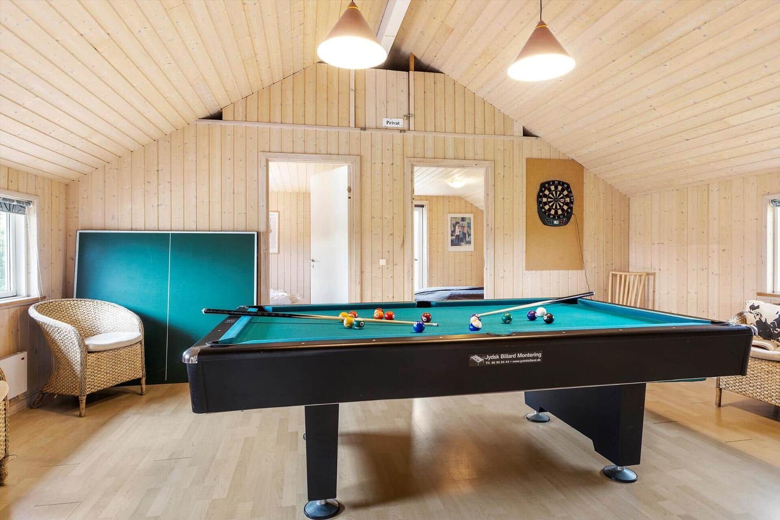 Raum mit Billardtisch, Dartboard und Tischtennisplatte. Holzwände und Decke.
