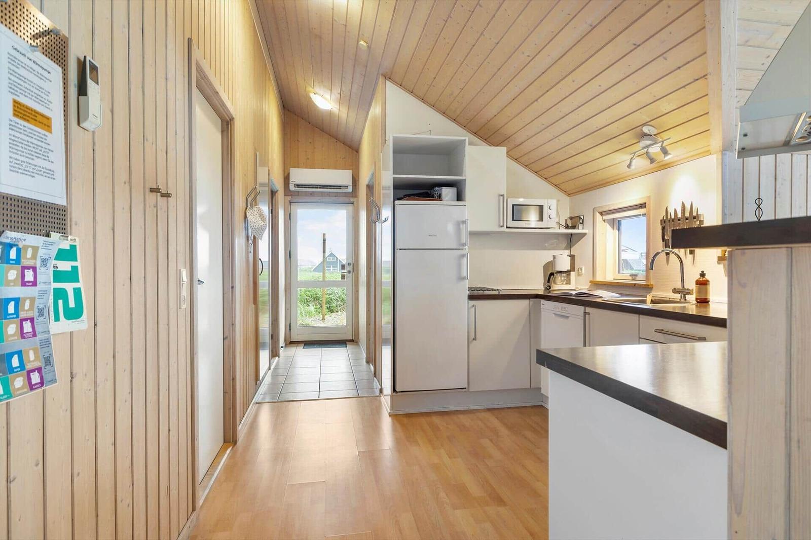 Küche mit Kühlschrank, Mikrowelle und Spüle. Holzdecke und -boden. Tür zum Außenbereich.