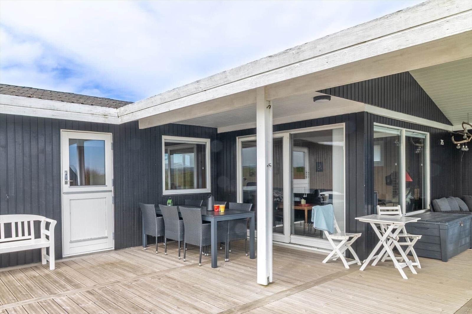 Terrasse mit Tisch, Stühlen und Sitzbank. Durchgehende Glasfront zum Innenraum.