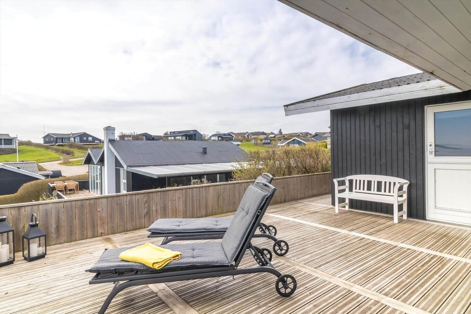 Terrasse mit Liegestühlen, weißem Stuhl und Blick auf Wohnhäuser.