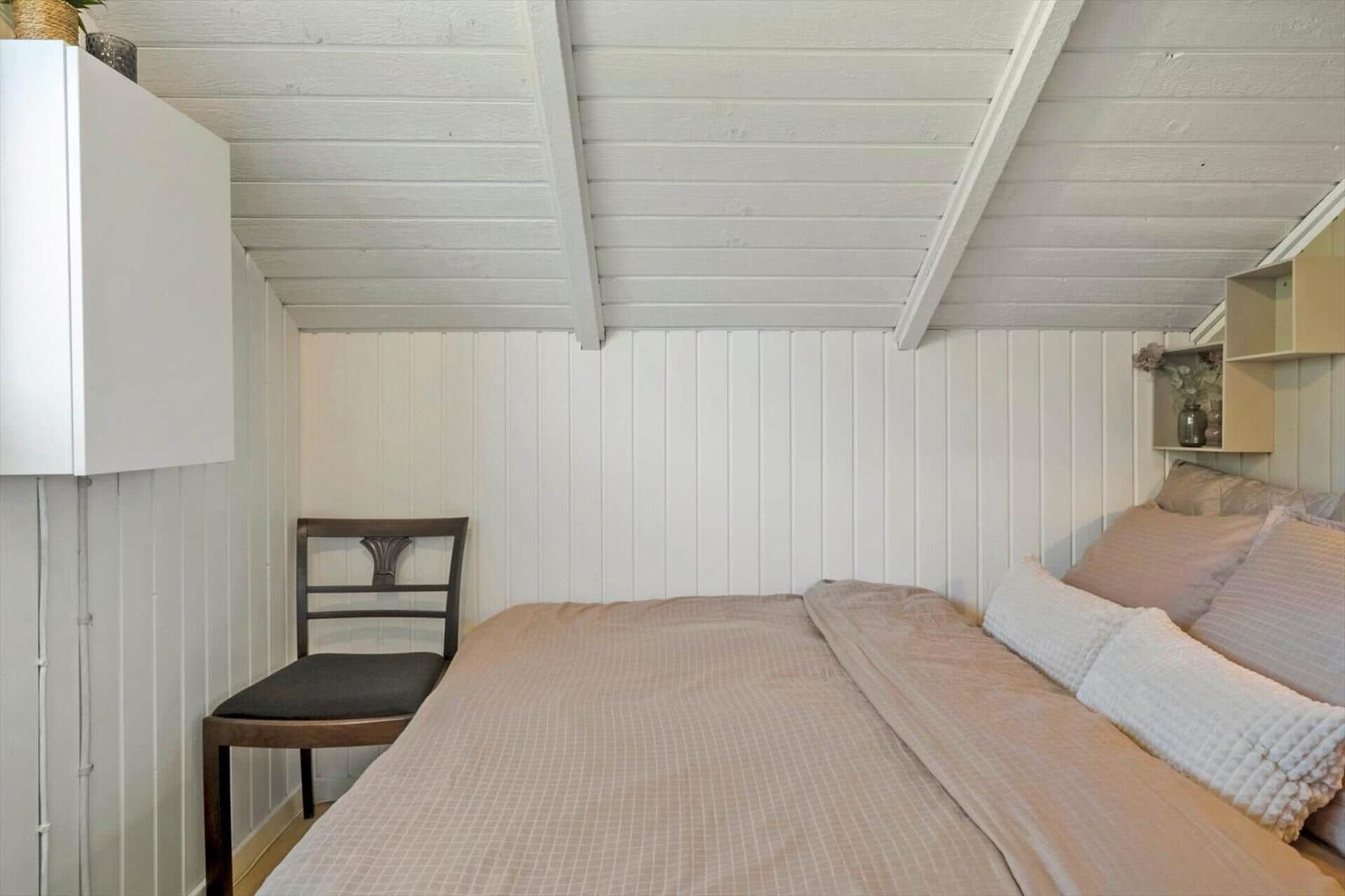 Schlafzimmer mit Bett, Stuhl und weißen Wänden unter schrägem Dach