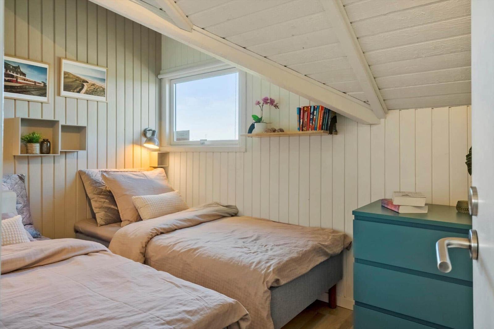 Zwei Betten unter Dachschrägen mit Fenster, Schrank und Wandregalen.