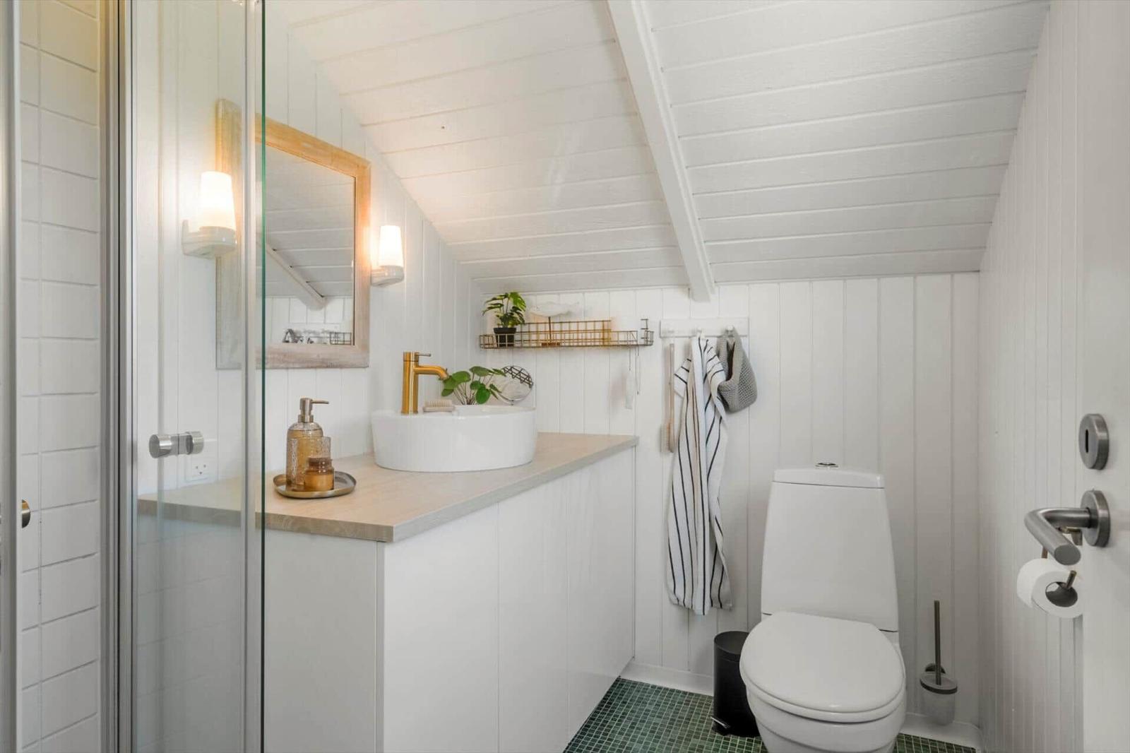 Badezimmer mit Dusche, Waschbecken und Toilette. Weiße Wände, grüner Boden und goldener Wasserhahn.