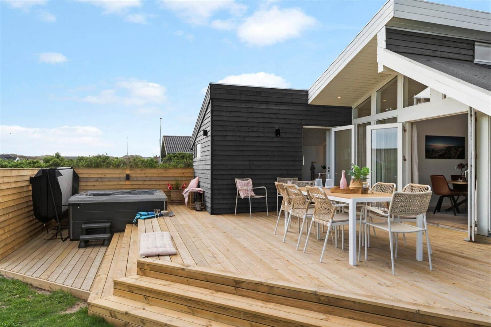 Terrasse mit Sitzgruppe, Esstisch und Whirlpool. Modernes Haus mit Glasfront.