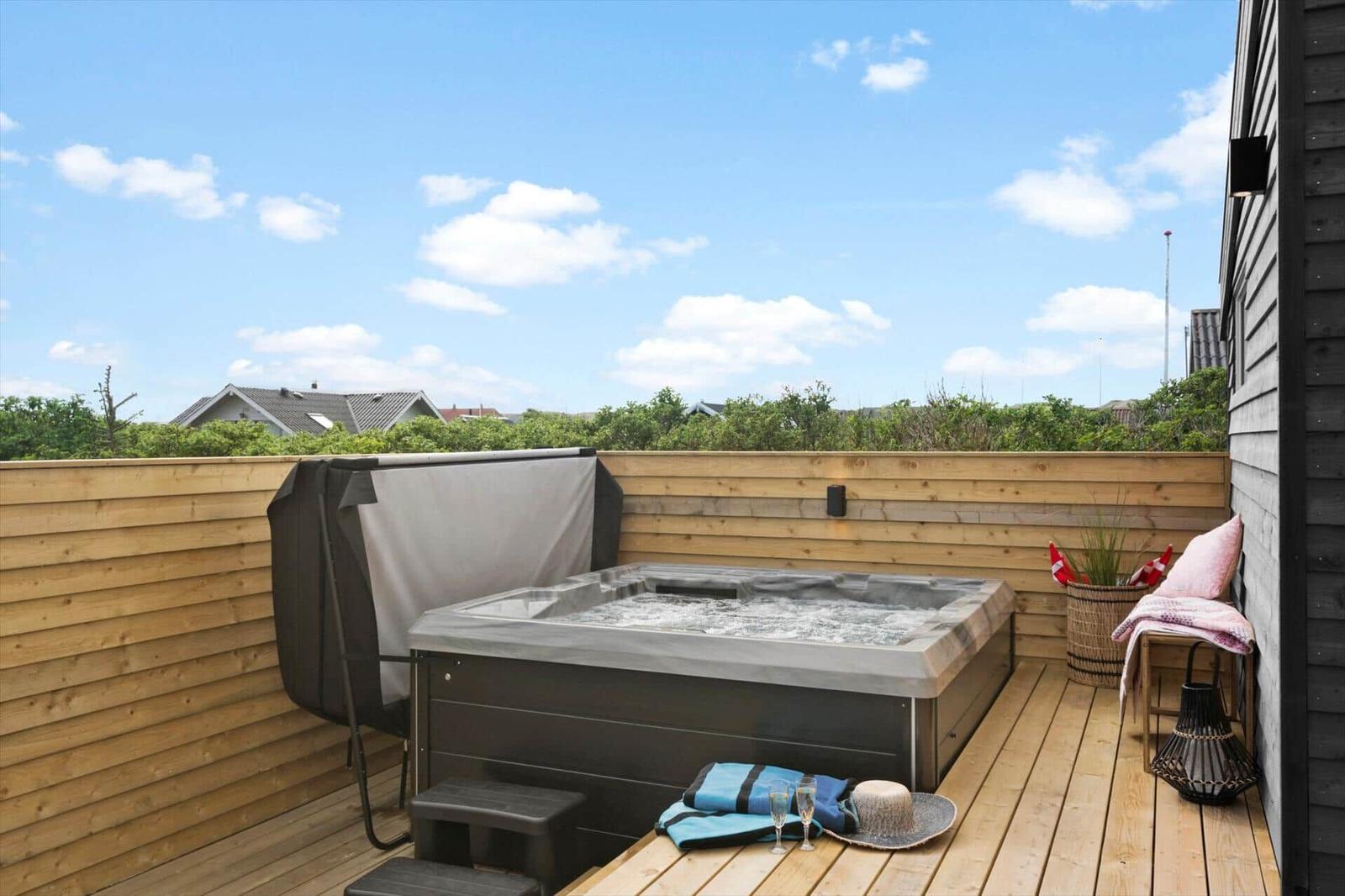 Terrasse mit Whirlpool, Holzgeländer und Blick auf Grünflächen.