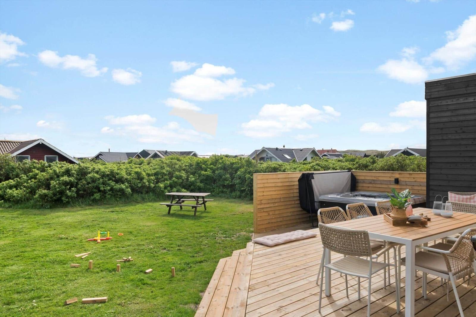 Holzterrasse mit Sitzgelegenheit und Grill. Grünflächen, Picknicktisch und Spielzeug im Garten.